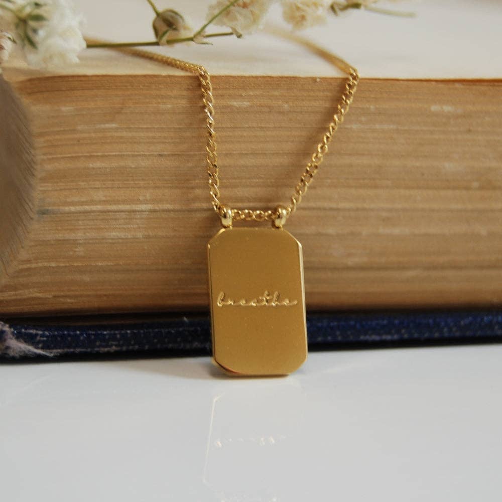 Gold necklace with a tag on a white surface with a book and flowers in the background