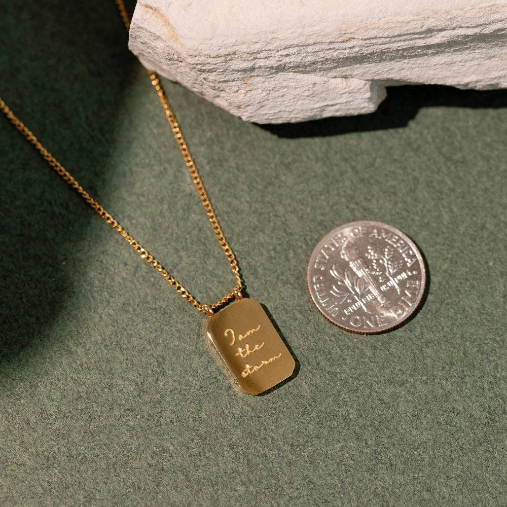 Gold necklace with a dog tag and engraved text, next to a U.S. quarter on a green surface.
