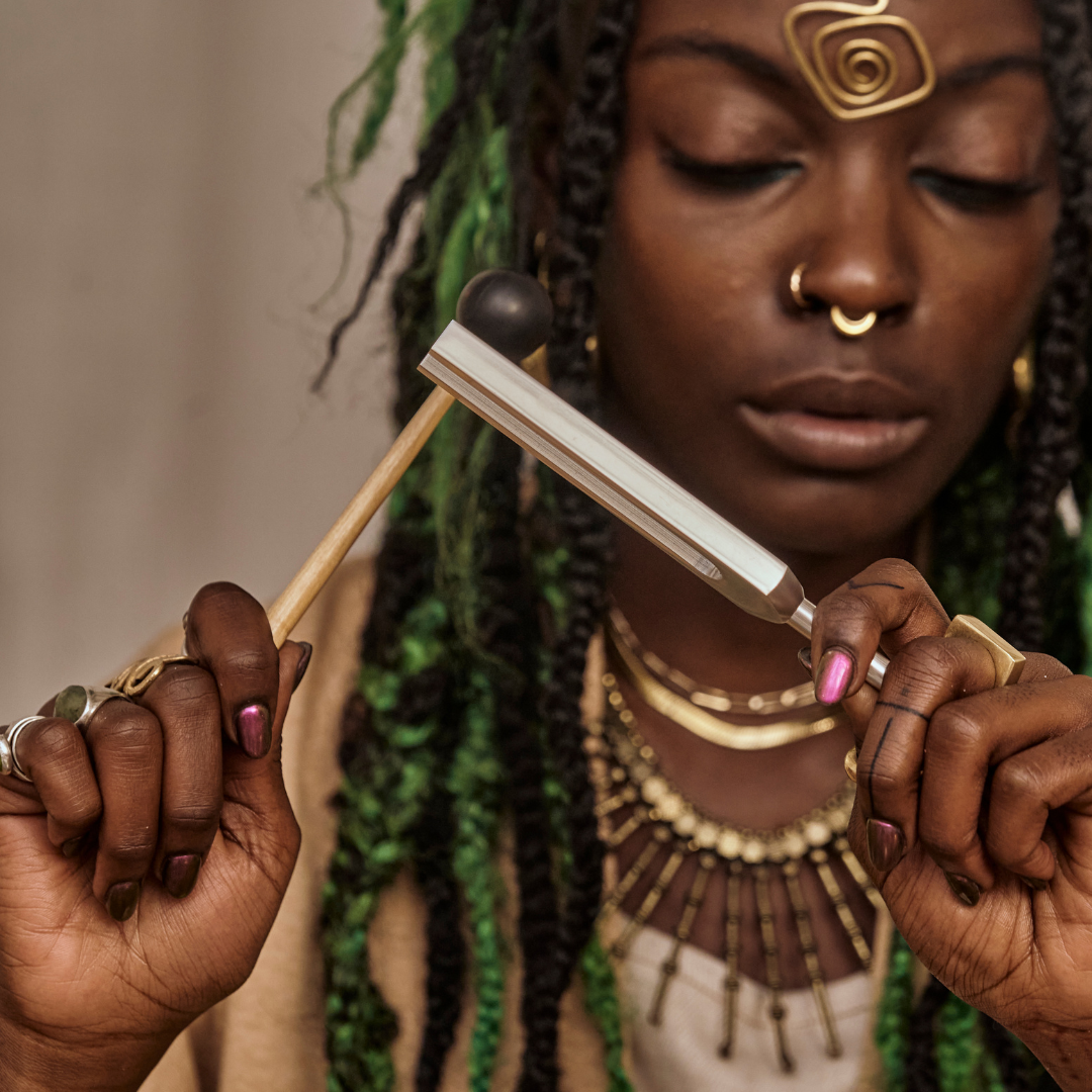 777 Hz Peace Tuning Fork: Woman with braided hair and gold jewelry holding a traditional tool