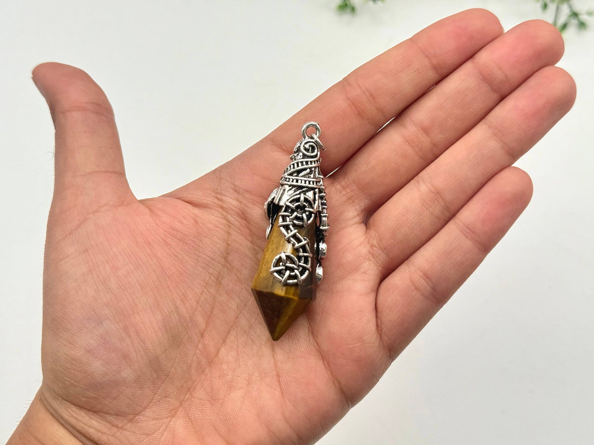Hand holding a crystal pendant with intricate design on a plain background