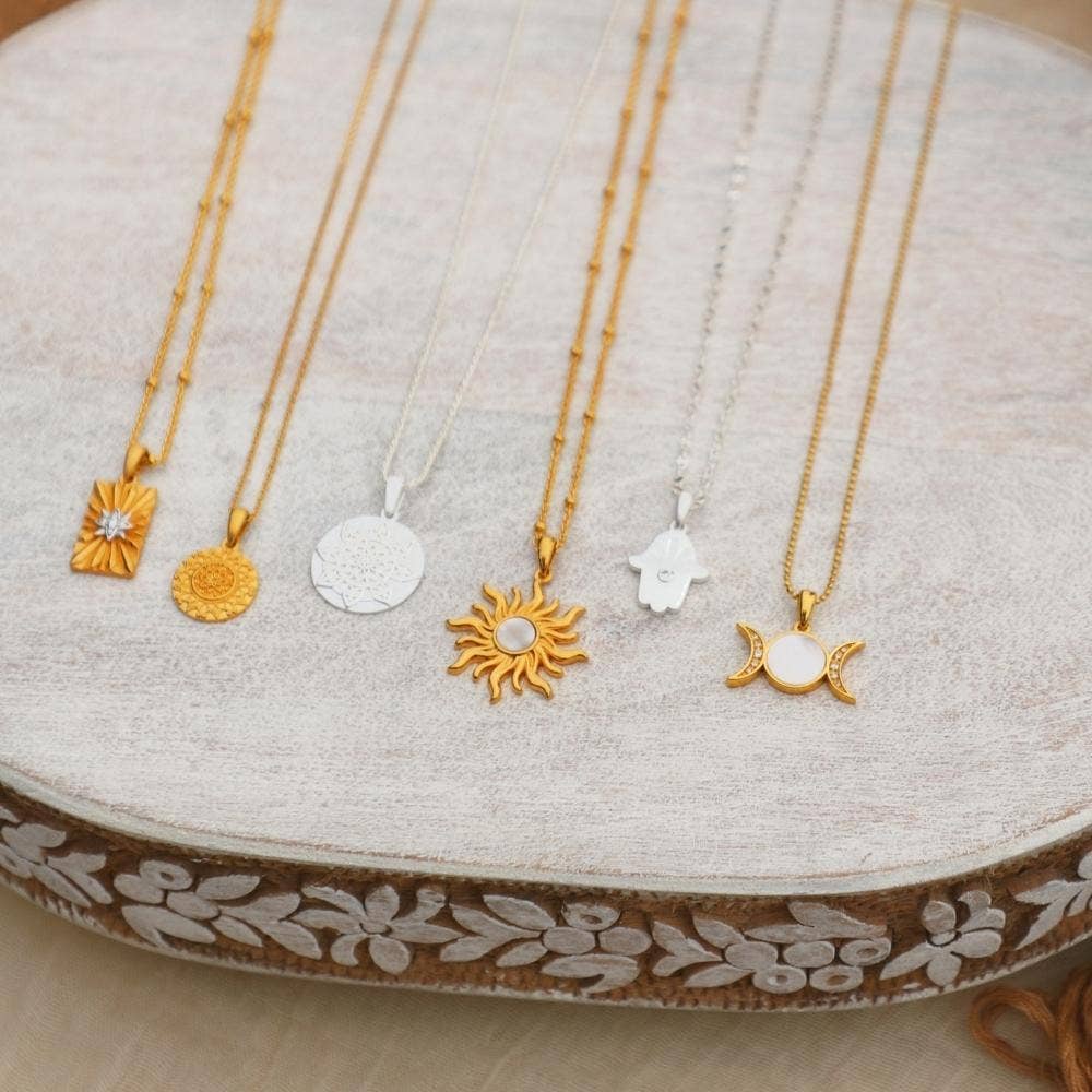 Five gold and silver necklaces with various pendants on a decorative wooden stand.