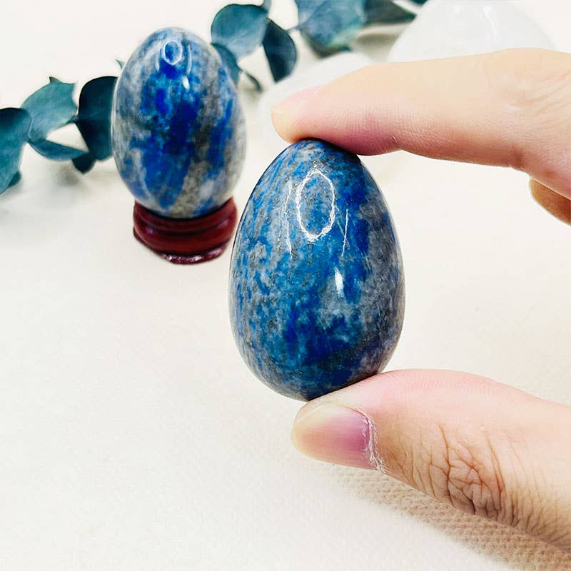 Blue and white speckled stone held by a hand with eucalyptus leaves in the background