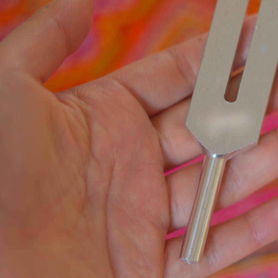 Hand holding a tuning fork against a colorful background