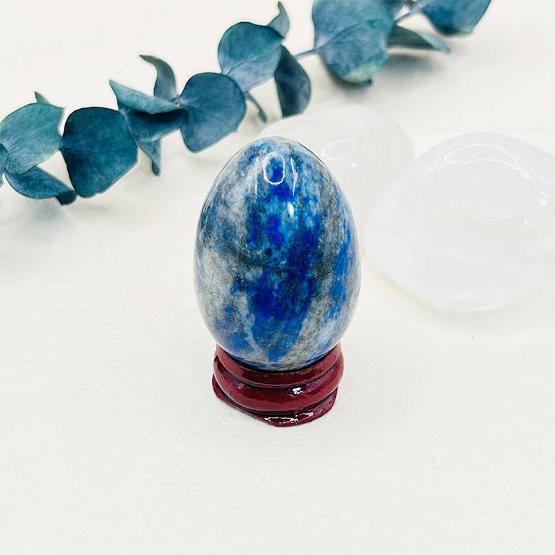 Blue and white marbled egg-shaped object on a red stand with eucalyptus leaves in the background.