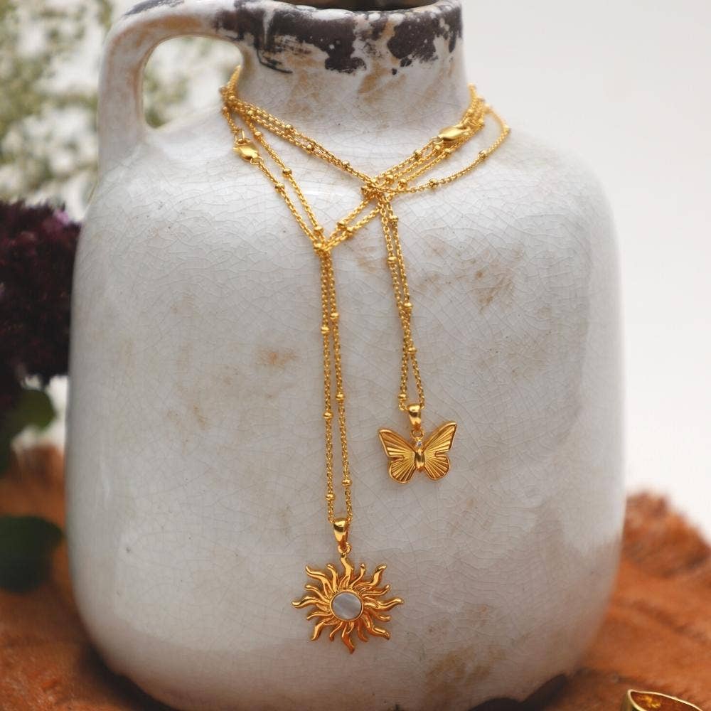 Gold necklaces with butterfly and sun pendant on a textured white surface