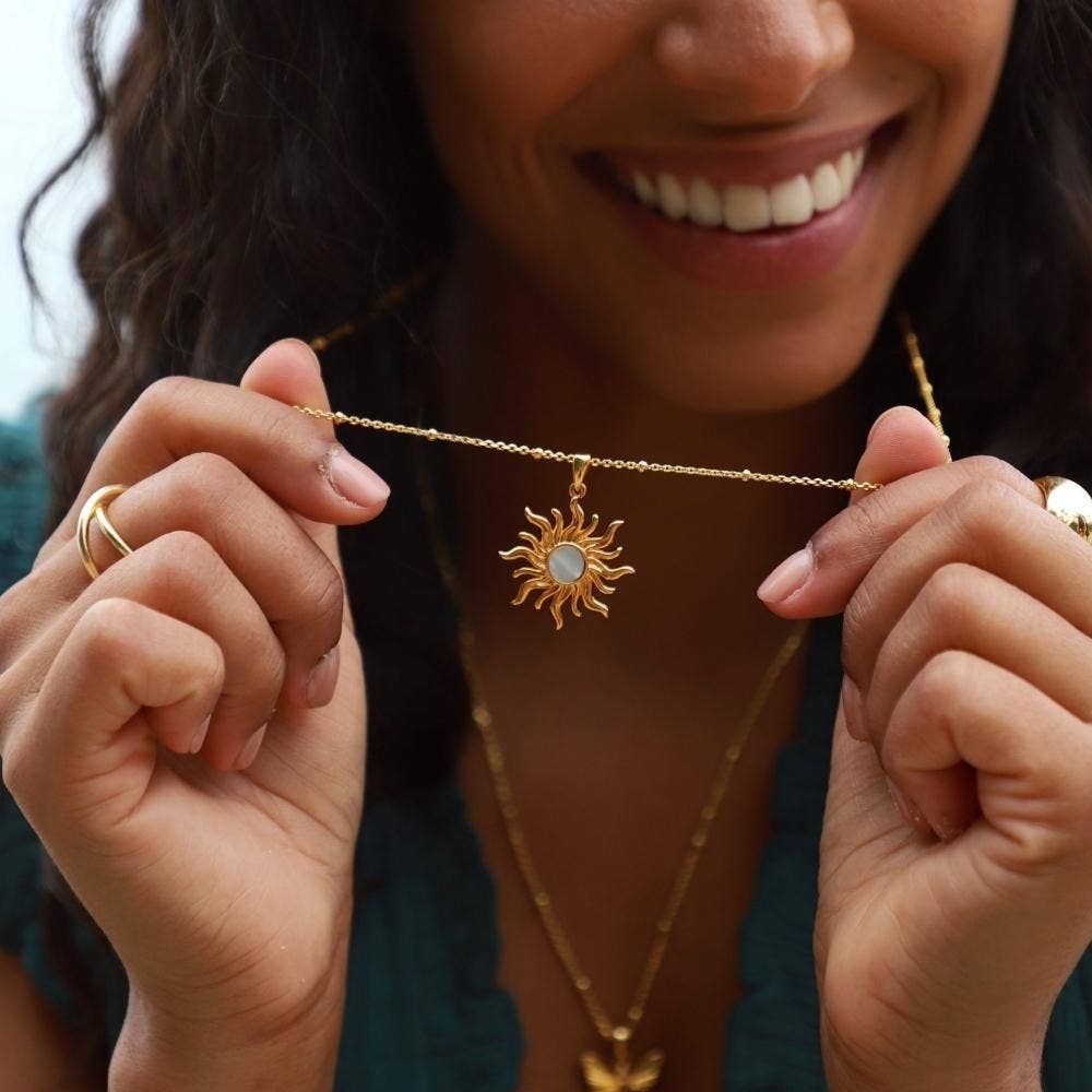Person holding a gold necklace with a sun pendant