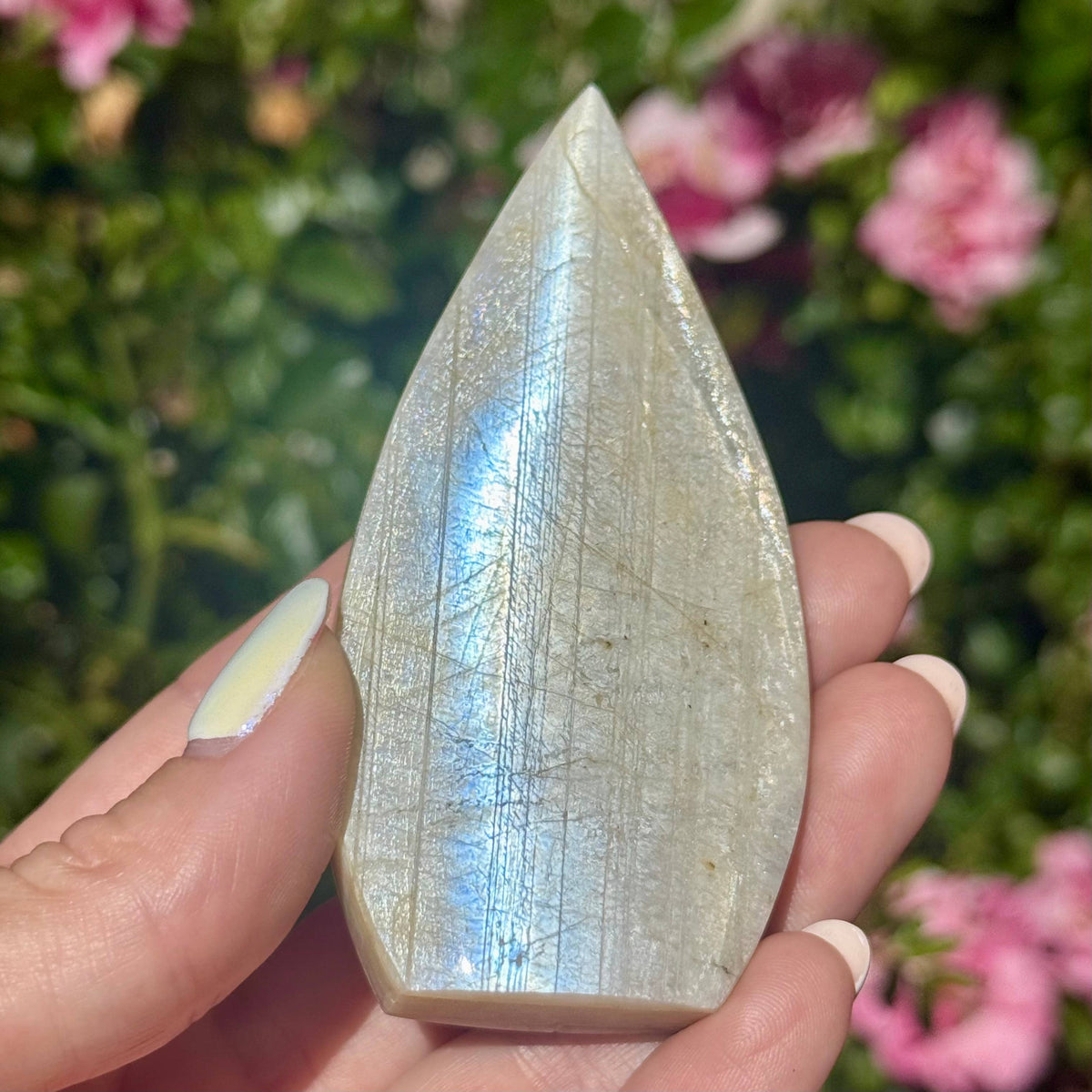 Teardrop-shaped crystal held in a hand with a blurred floral background