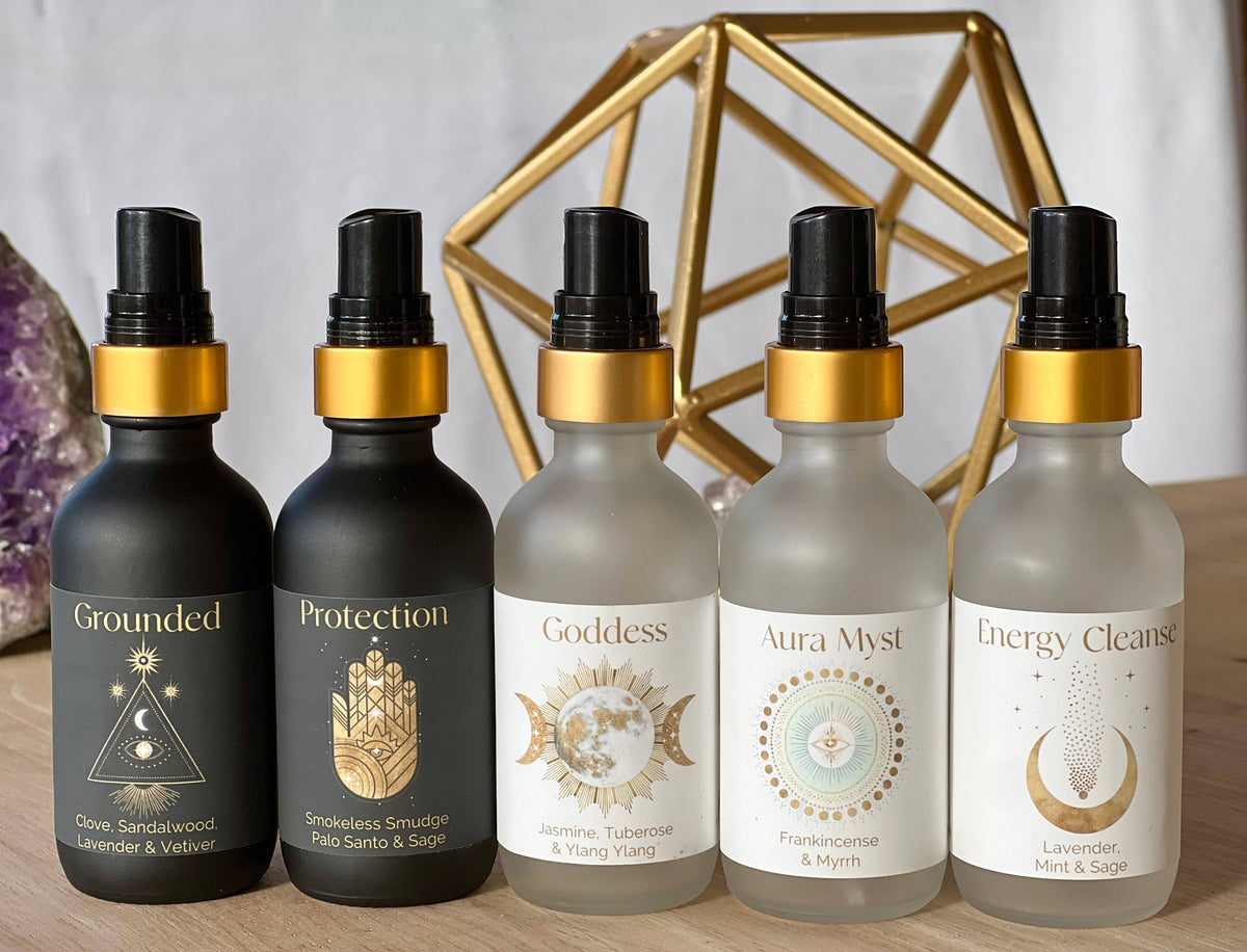 Five bottles with black and gold caps on a wooden surface, with geometric and crystal decorations in the background.