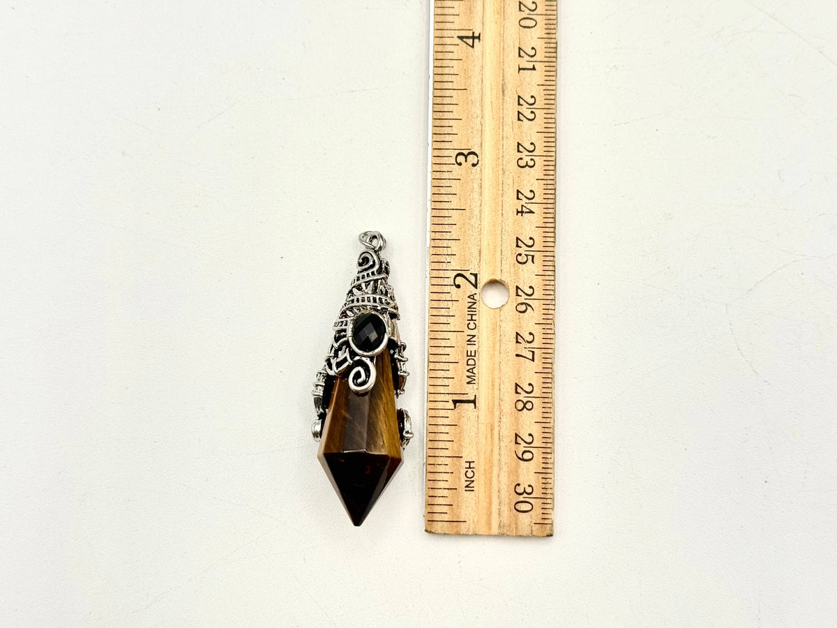 Pendant with a black stone and silver detailing next to a wooden ruler on a white background
