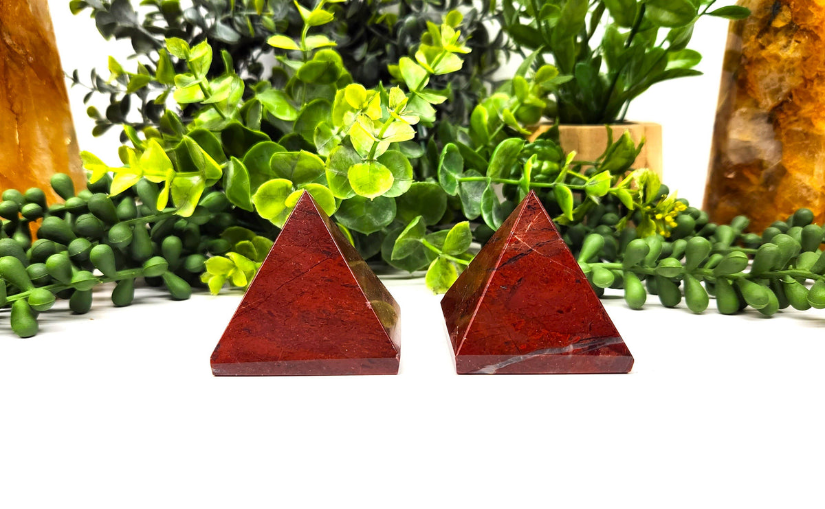 Two red pyramids on a white surface with green plants in the background