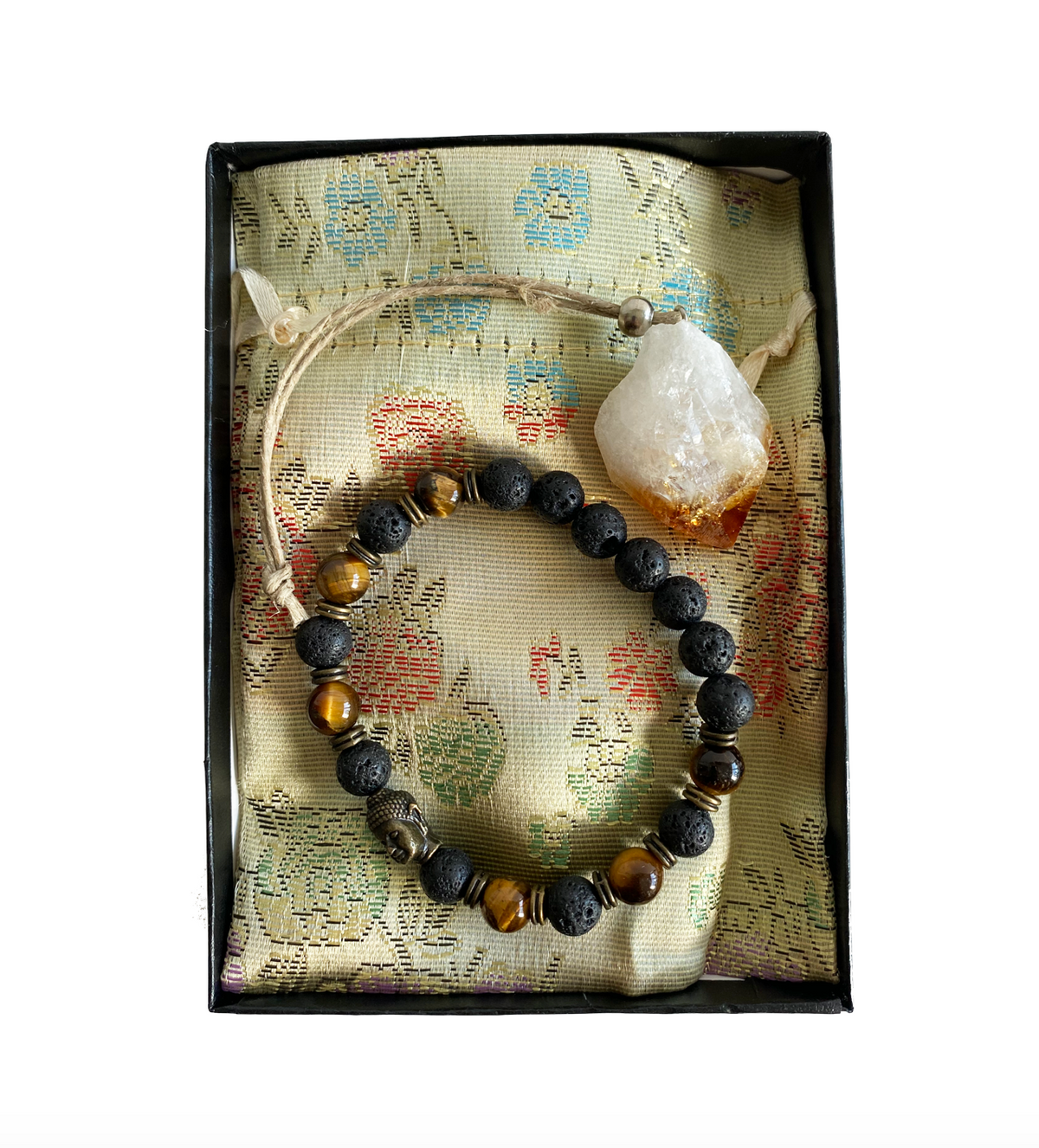 A gift box containing a bronze Buddha figure with tiger's eye beads and a citrine stone, all placed on a fabric with a floral pattern - JOY - Journey Of You - Spiritual, Holistic, Empowering