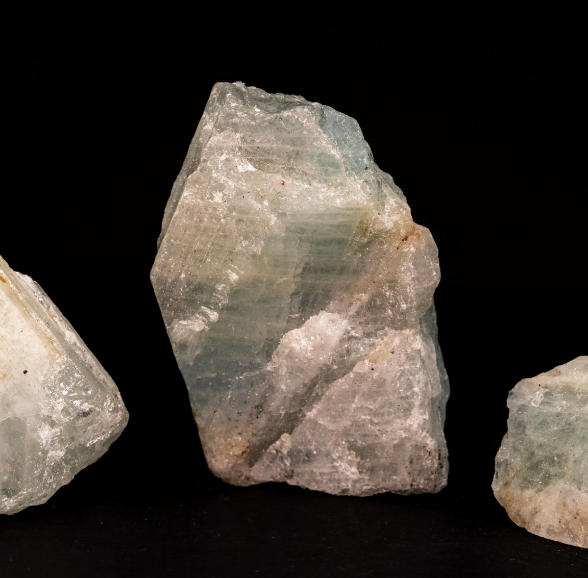 Three Raw Aquamarine Crystal of varying sizes displayed against a black background. 