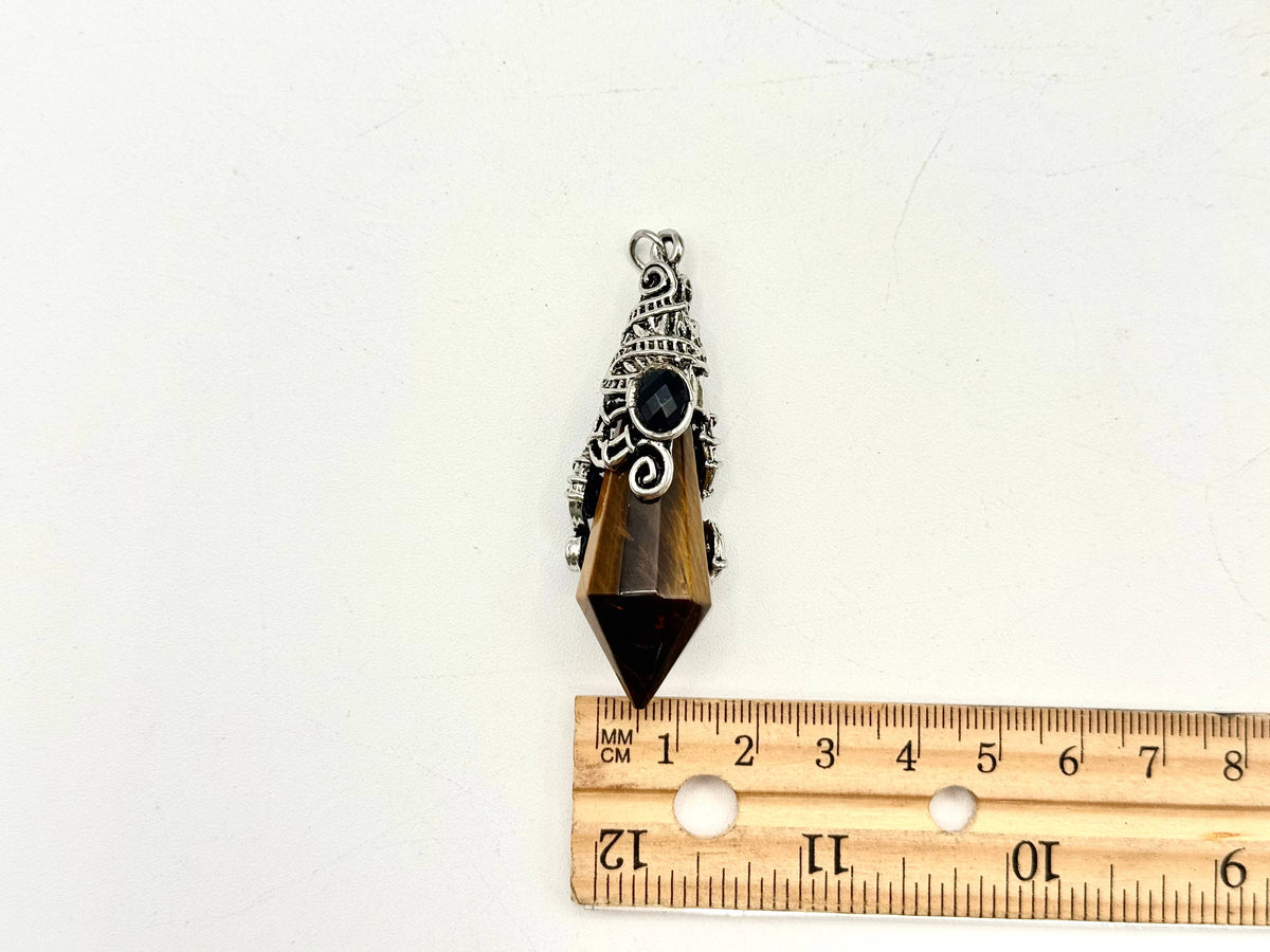 Pendulum with decorative elements on a white background next to a wooden ruler for scale.