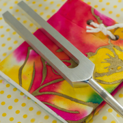 Metal tuning fork on a colorful tie-dye background with yellow polka dots