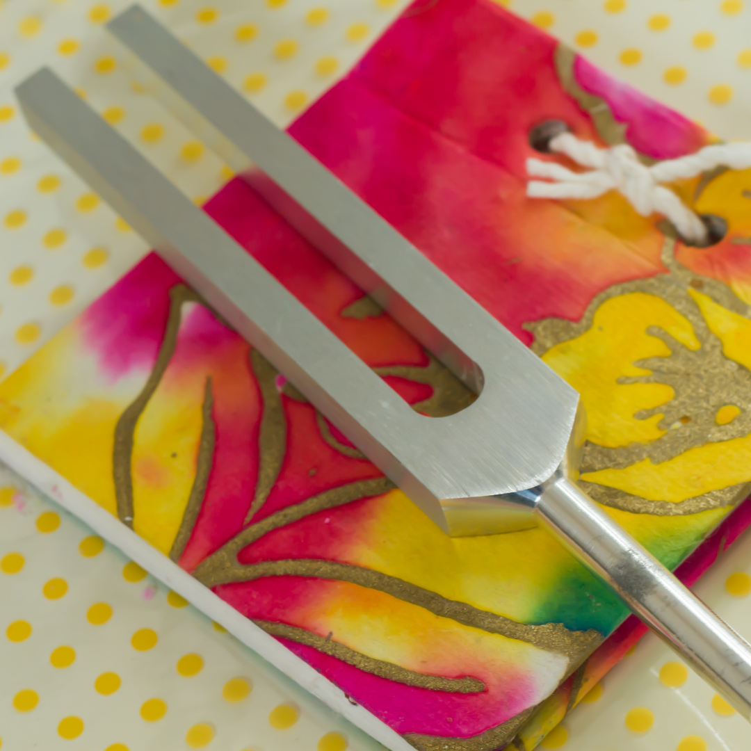 Metal tuning fork on a colorful tie-dye background with yellow polka dots