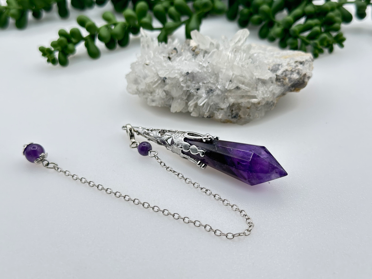 Amethyst crystal necklace with silver chain on a white surface with greenery