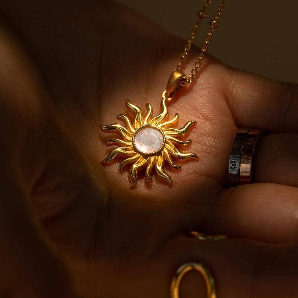 Gold sun-shaped pendant on a chain held in a hand.