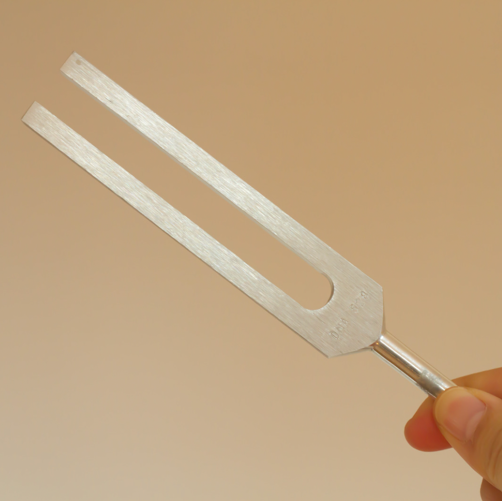 Metal tuning fork held by a hand against a beige background