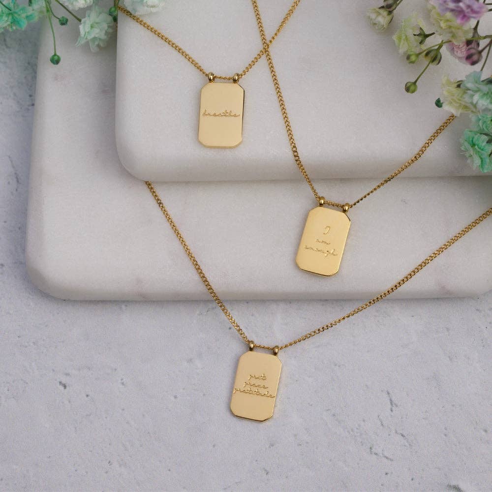 Gold necklaces with engraved dog tags on a light gray surface with floral elements.