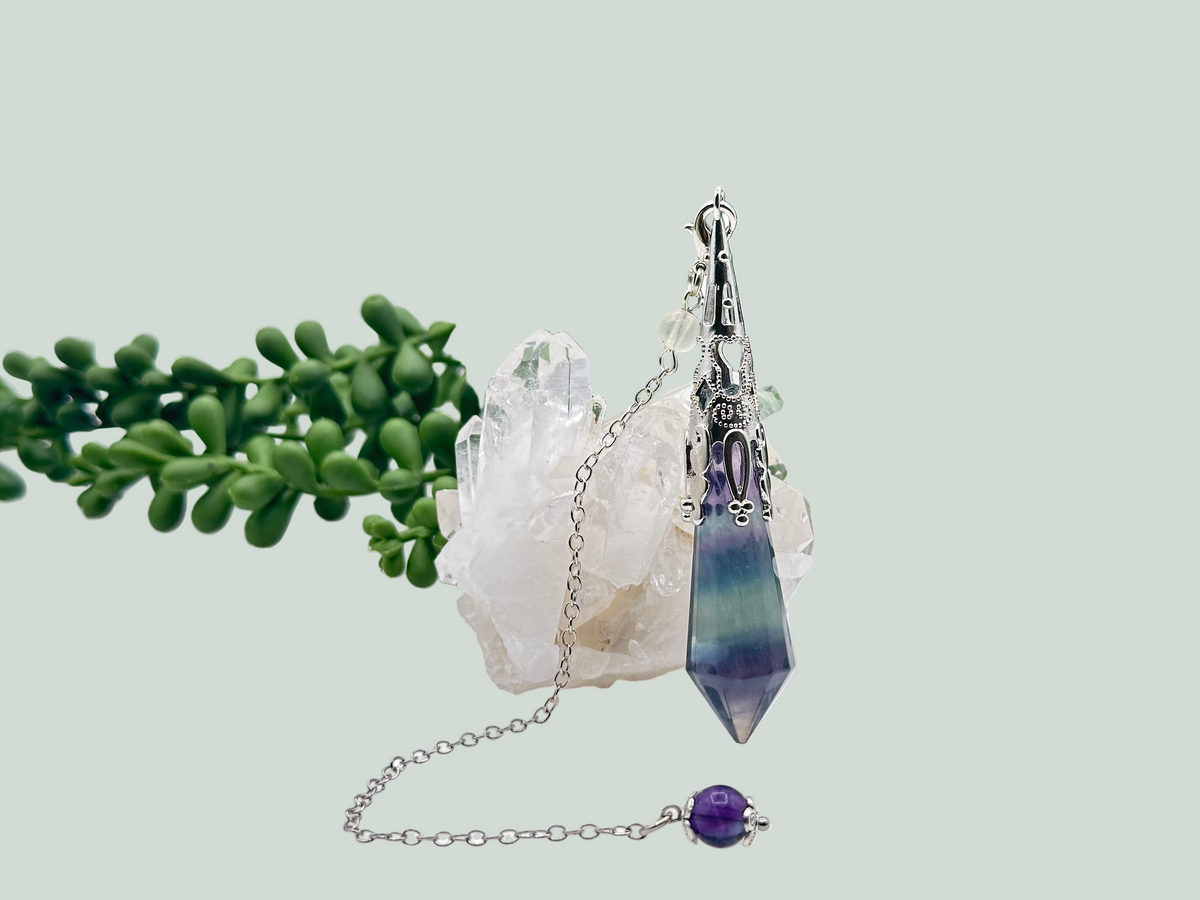 Crystal necklace with a purple pendant on a white surface with greenery