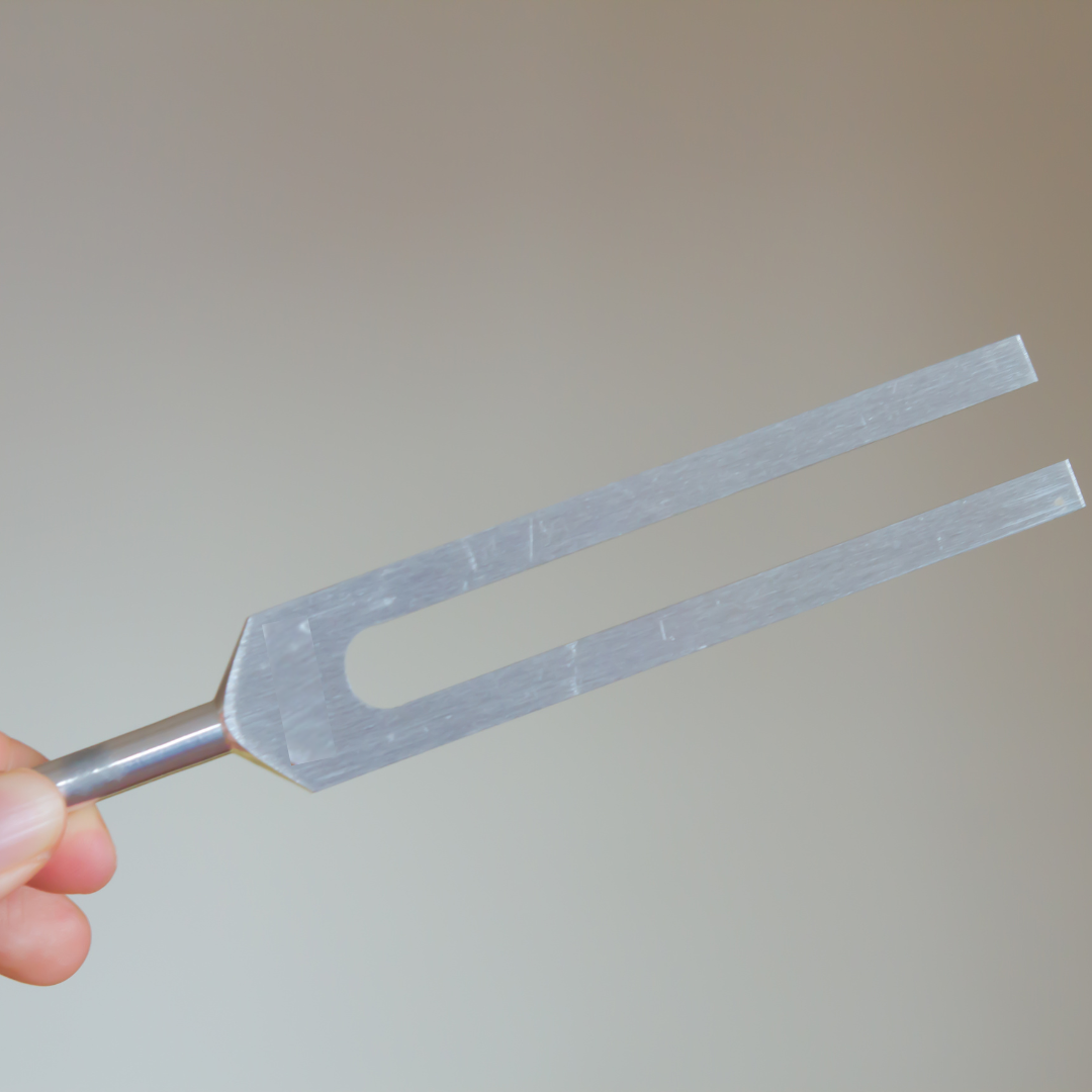 Tuning fork held by a hand against a plain background