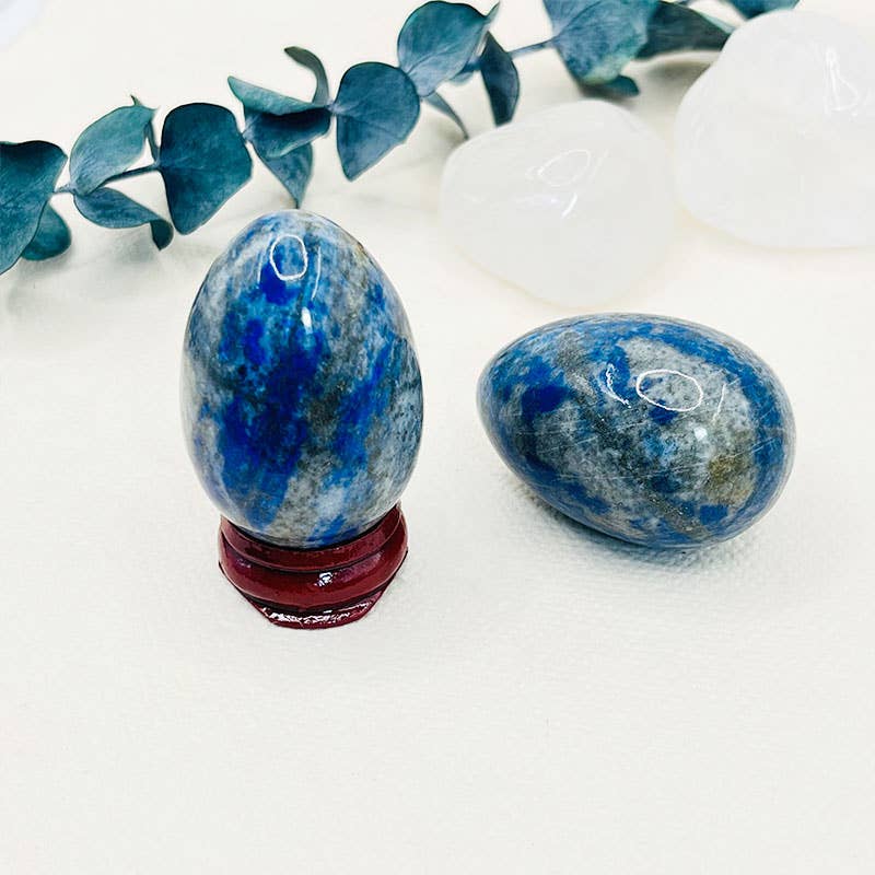 Two blue stone eggs on a white surface with green leaves in the background